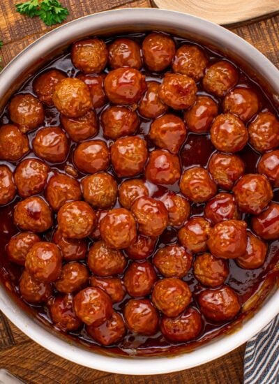 Peach BBQ Meatballs in a skillet on a wooden table with parsley to the side of it