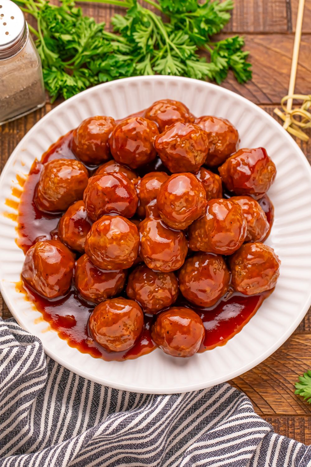 white plate full of Peach BBQ Meatballs sitting on table with a towel in front and parsley behind the plate
