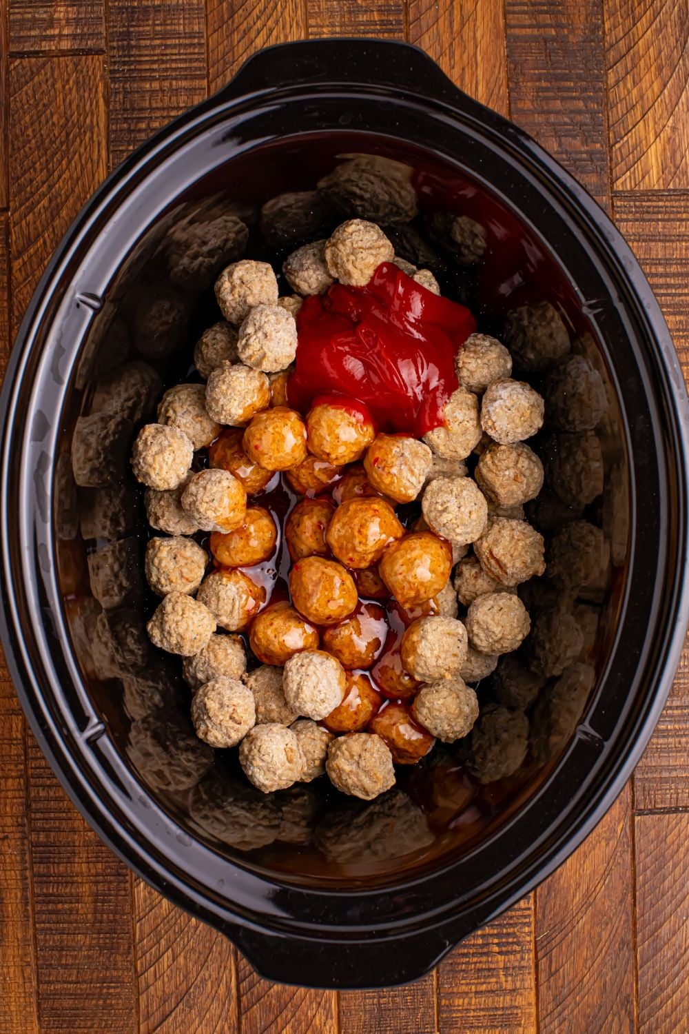 frozen meatballs in a black crockpot with sauce poured in it 