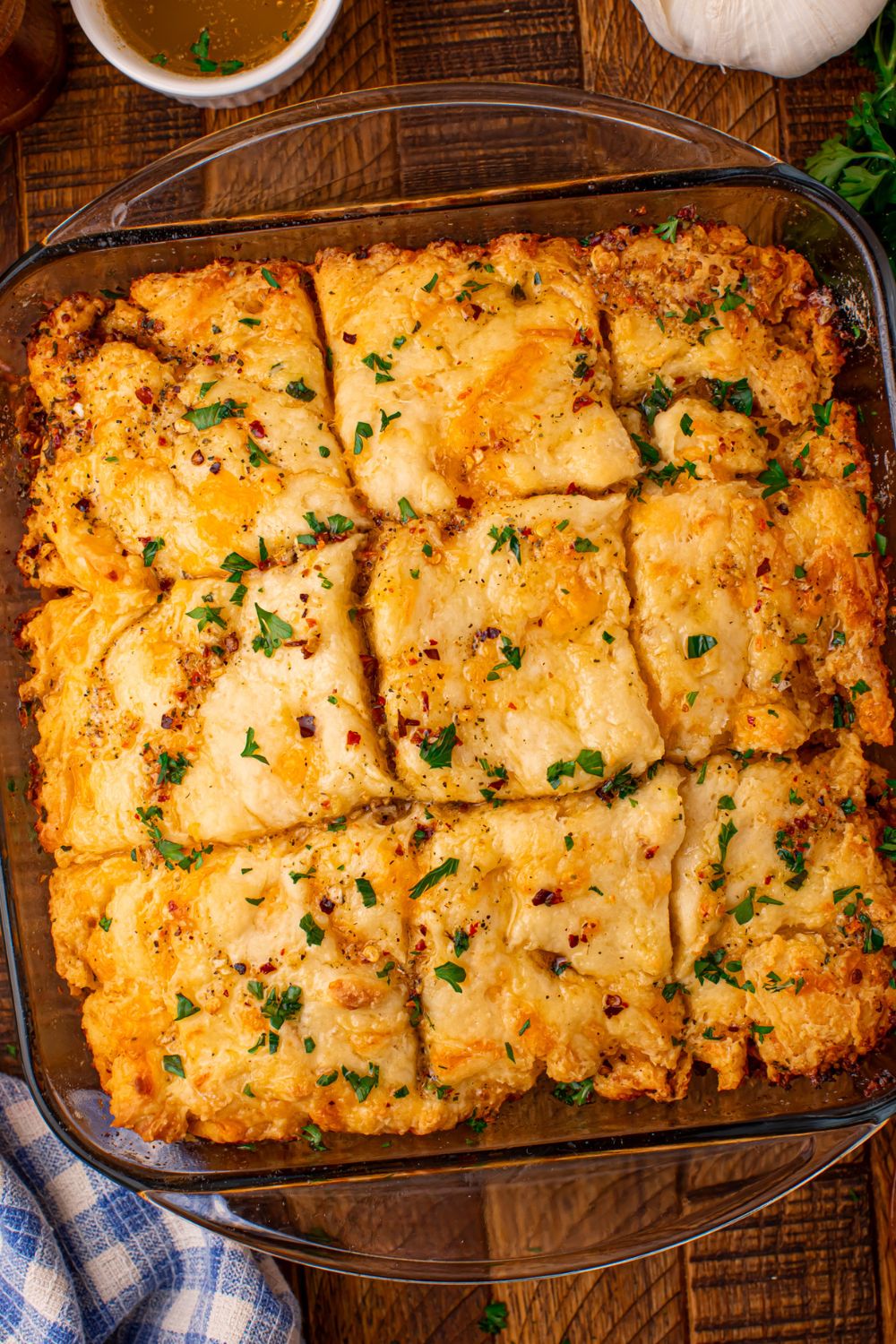 looking down on table and a 8x8 pan full of soft butter biscuits with herbs and spices and garlic and cowboy butter to the side