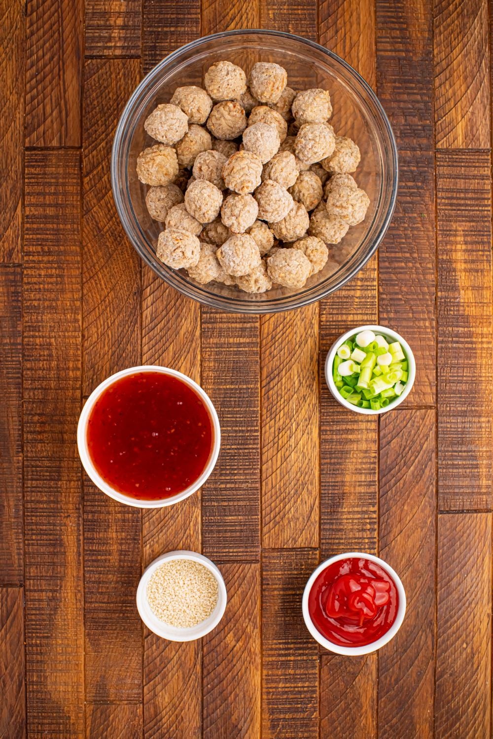a glass bowl of frozen meatballs on wooden table with sweet chili sauce, green onions all in single serve bowls on the table 