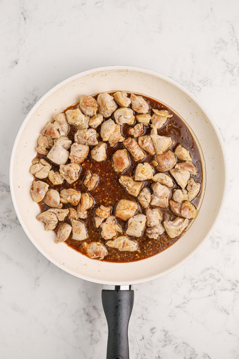 diced chicken cooked and poured with sauce in a skillet on table 