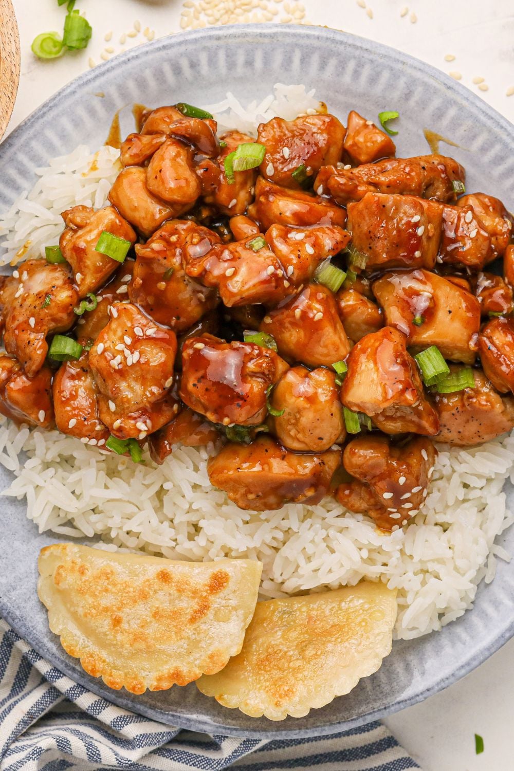 Bourbon Chicken close up on plate with a bit of rice and topped with sesame seeds and green onions on top 
