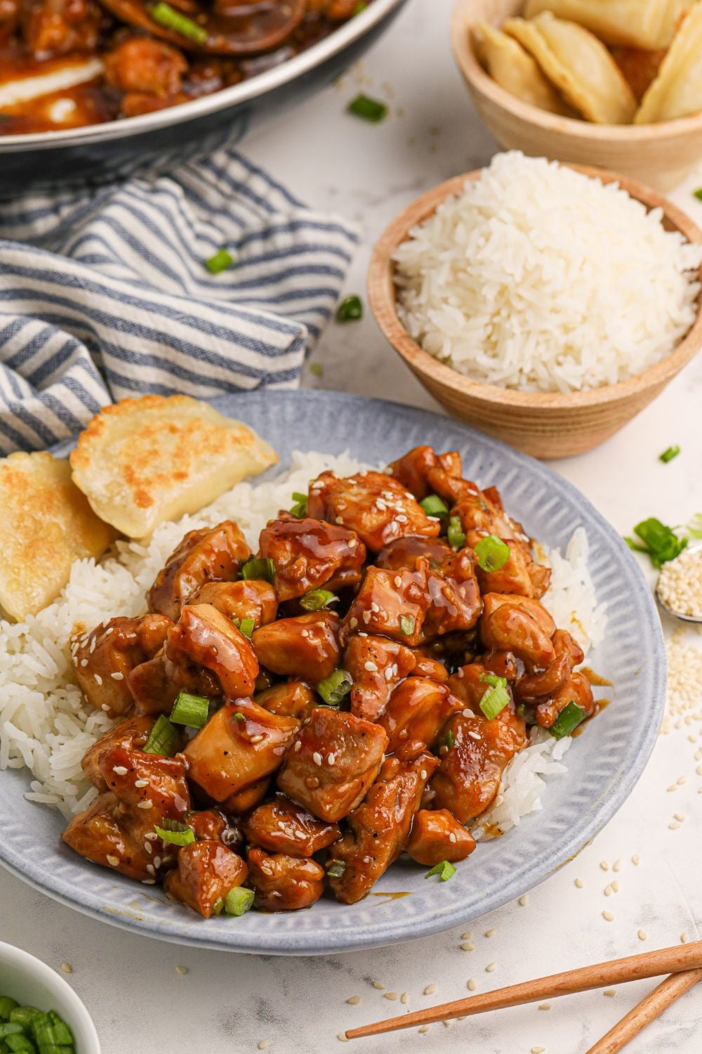 Bourbon Chicken  on a plate with rice to side and bread, with a bowl of rice and more chicken spread out on the table 