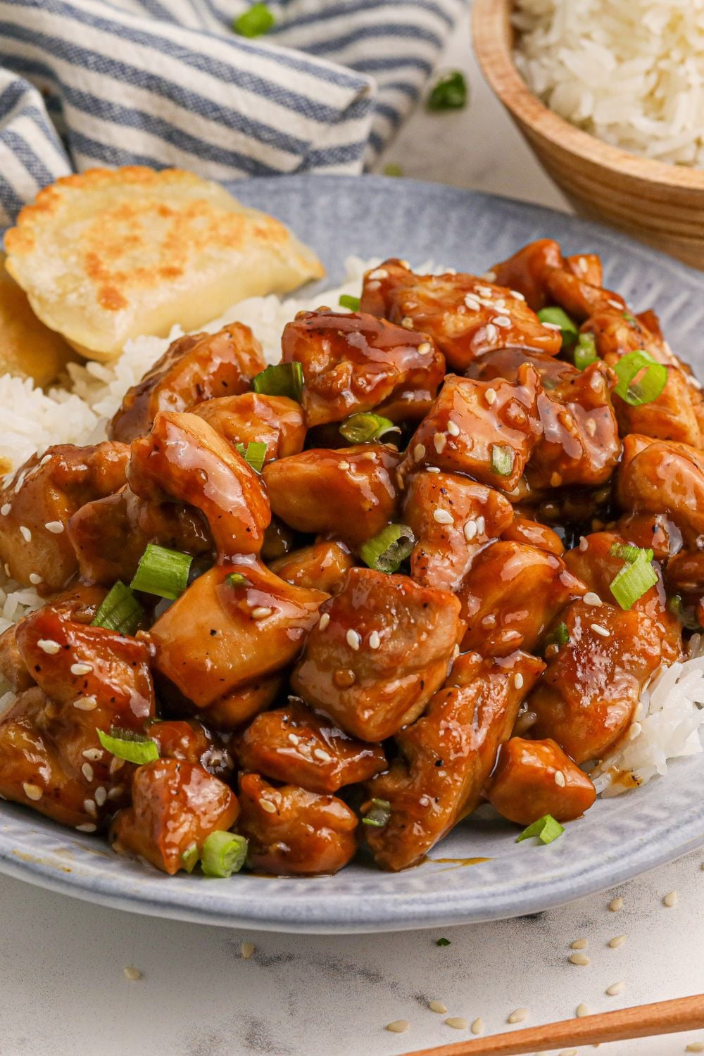 a blue and white plate on table with diced bourbon chicken and white and pieorgies to the side on the the 