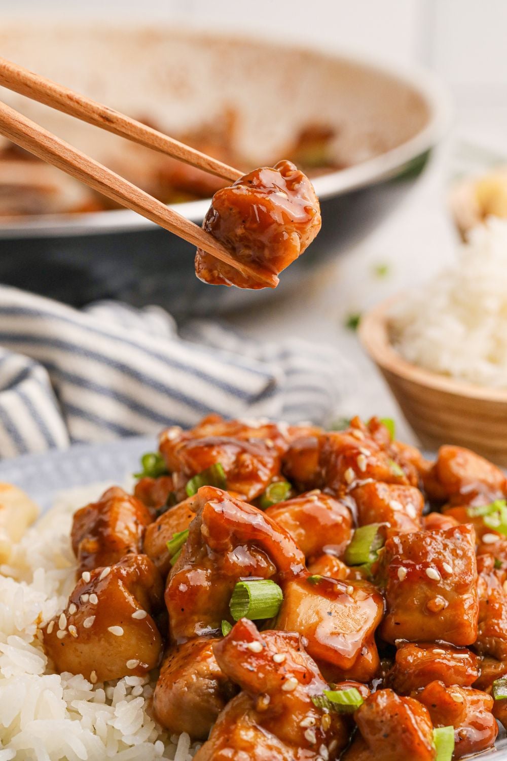 Bourbon Chicken on a plate with some chopsticks lifting a piece of chicken out of the plate 