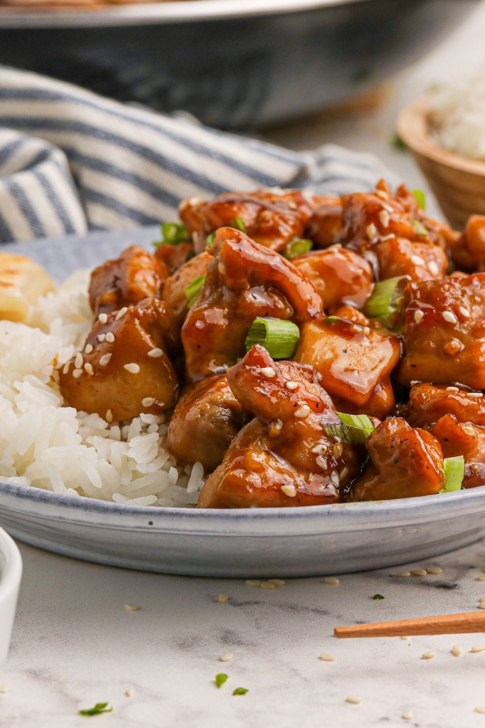 plate with some diced bourbon chicken ad a side of rice to side with a striped grey towel behind it on the table