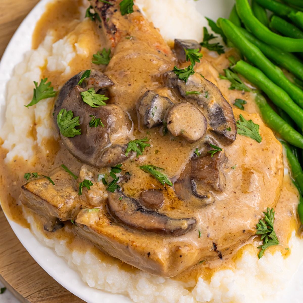 Crockpot Smothered Pork Chops with Mushroom Gravy on a plate with mashed potatoes and green beans 