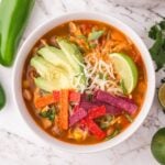 Southwestern Chicken Soup in a white bowl topped with tortilla chips, avocado, lime wedge, and more