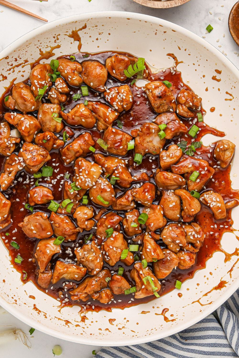 side view of a white skillet on table full of saucy bourbon chicken 