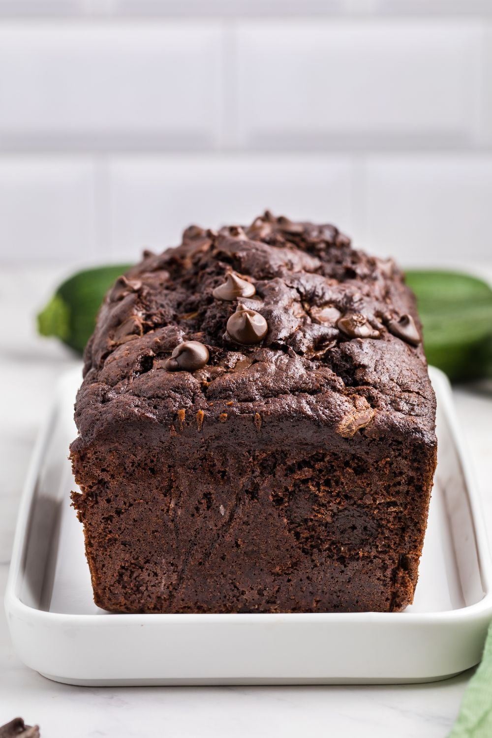 Double Chocolate Zucchini Bread on a white platter sitting on a counter with zucchini in the background