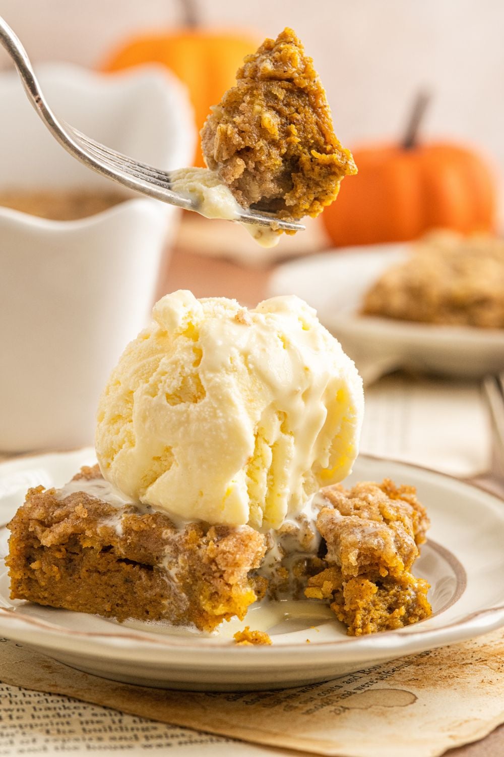 Homemade Pumpkin Crisp on a plate with ice cream on top and a bite being lifted up off the table on fork