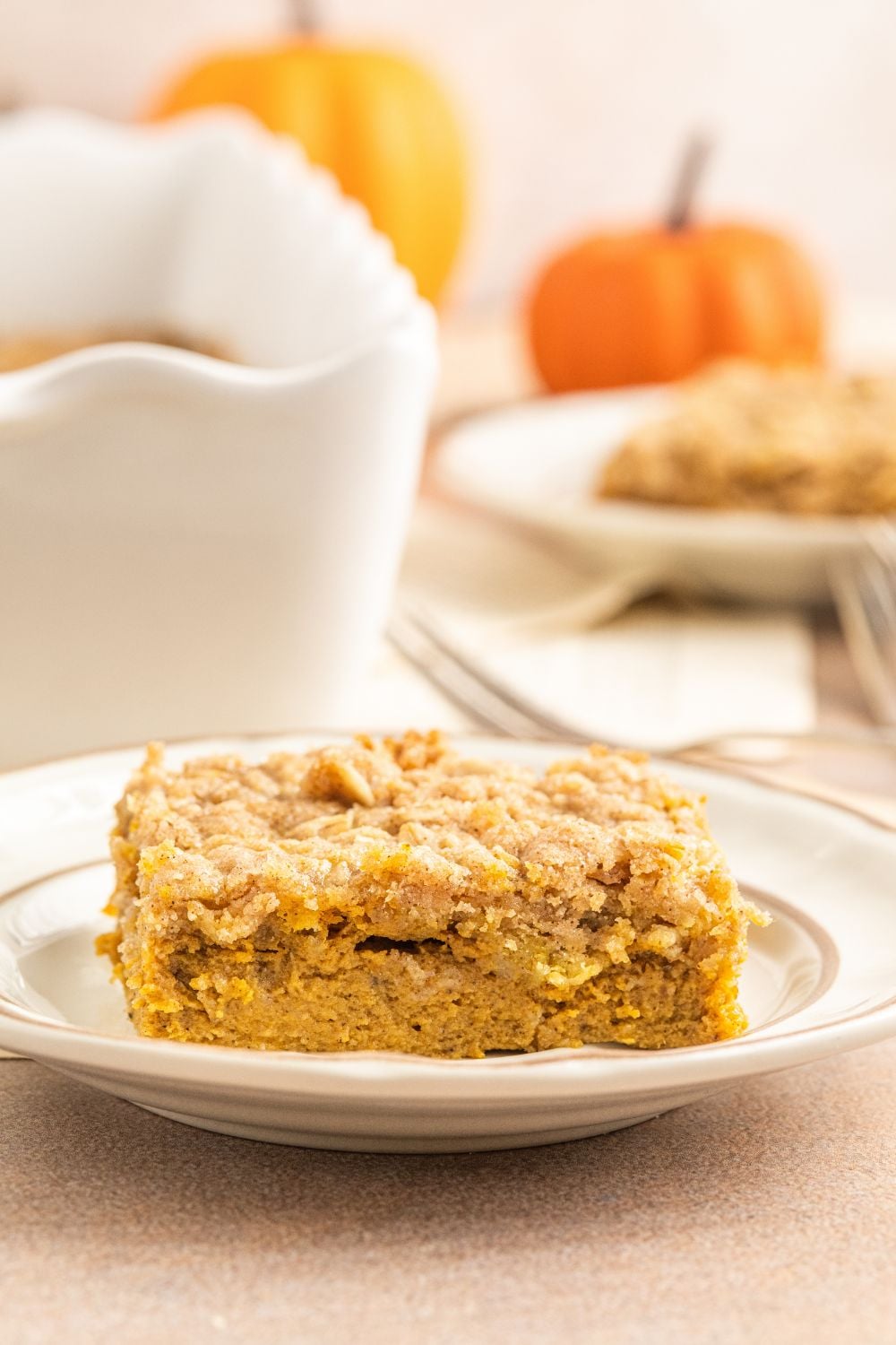 Homemade Pumpkin Crisp is on a white plate sitting on the table with the other white casserole dish with more behind it on the table 