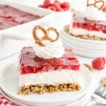 Raspberry Pretzel Salad on a white plate topped with a dollop of whipped cream and a pretzel on top