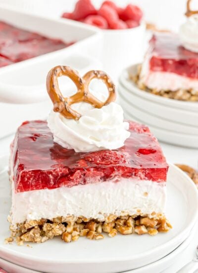 Raspberry Pretzel Salad on a white plate topped with a dollop of whipped cream and a pretzel on top