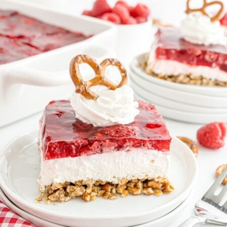 Raspberry Pretzel Salad on a white plate topped with a dollop of whipped cream and a pretzel on top